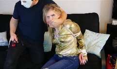 Dresden wearing a shiny golden blouse and jeans is a cowgirl held for ransom, cleave gagged and then ballgagged