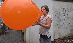 Simona inflates a giant orange balloon outside (4K quality)
